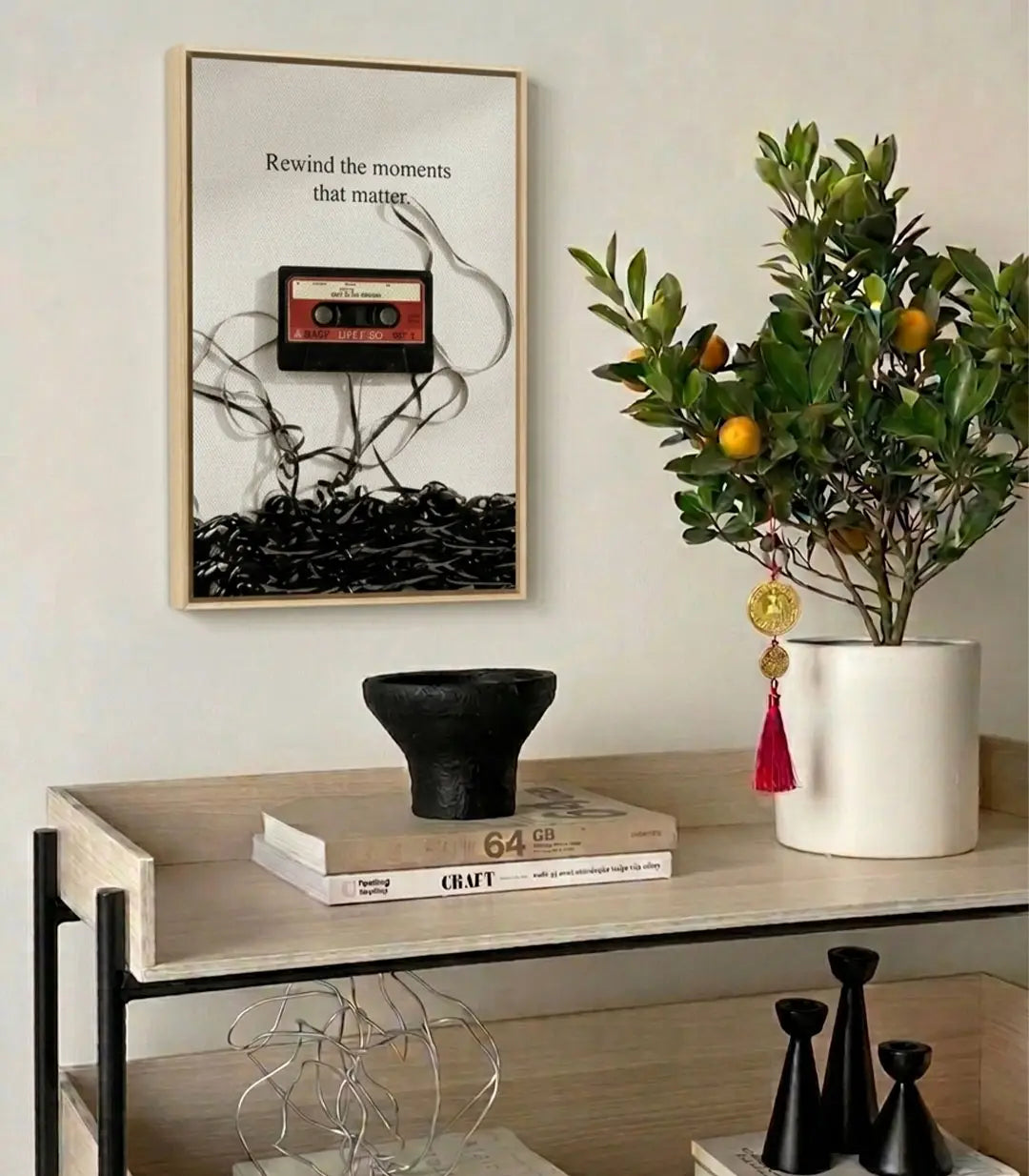 Decoración de despacho — cuadro casete vintage sobre pared blanca encima de estantería con libros y accesorios Massinart